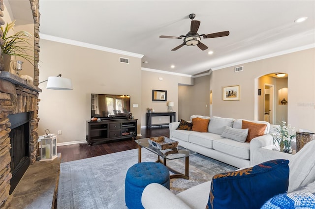 living area with wood finished floors, visible vents, arched walkways, ceiling fan, and a stone fireplace