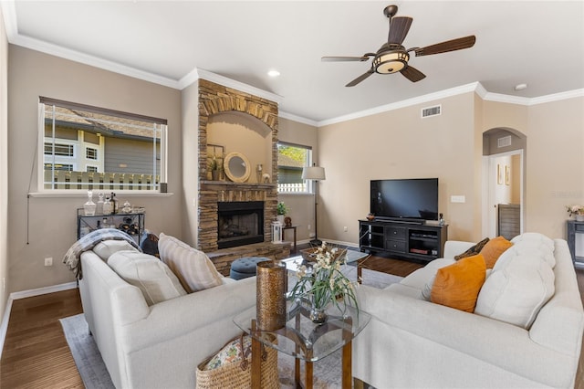 living area featuring a ceiling fan, wood finished floors, arched walkways, a stone fireplace, and baseboards