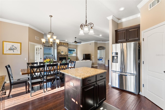 kitchen featuring visible vents, dark wood-type flooring, ceiling fan with notable chandelier, a fireplace, and stainless steel refrigerator with ice dispenser