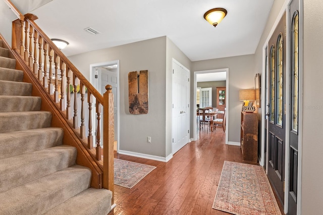 foyer entrance with visible vents, baseboards, hardwood / wood-style floors, and stairs