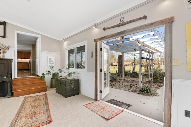 doorway to outside featuring vaulted ceiling, carpet flooring, a wainscoted wall, and ornamental molding