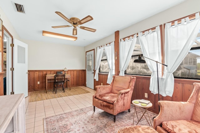 living area featuring visible vents, a wainscoted wall, wooden walls, tile patterned flooring, and ceiling fan