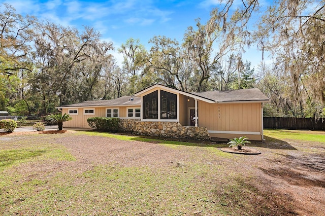 view of front facade featuring stone siding, a front yard, and fence