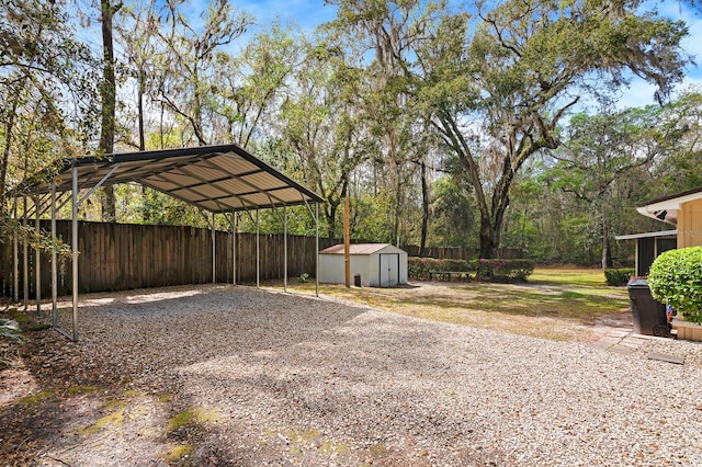 view of yard with fence, a carport, driveway, a storage unit, and an outbuilding