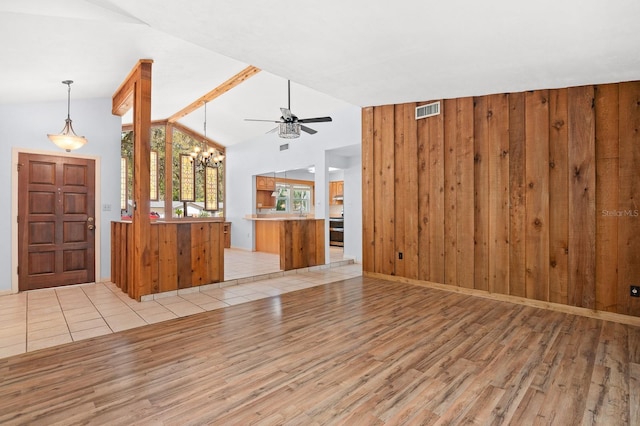 unfurnished living room with lofted ceiling, wooden walls, light wood-style floors, and visible vents