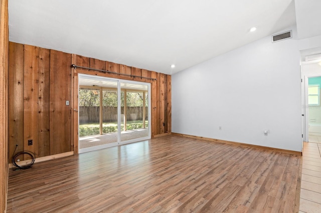 unfurnished room featuring light wood finished floors, visible vents, wooden walls, baseboards, and recessed lighting