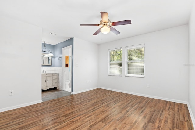 unfurnished bedroom with visible vents, wood finished floors, baseboards, and ensuite bathroom