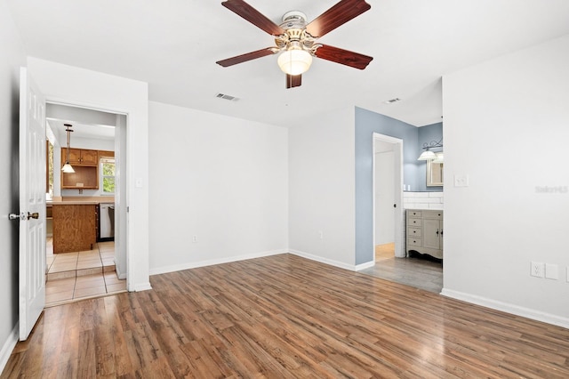 unfurnished bedroom featuring wood finished floors, visible vents, baseboards, ensuite bath, and ceiling fan