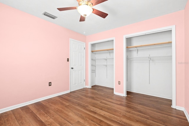 unfurnished bedroom featuring visible vents, multiple closets, wood finished floors, baseboards, and ceiling fan