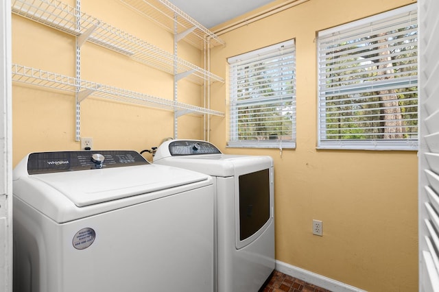 clothes washing area featuring laundry area, washing machine and dryer, brick floor, and baseboards