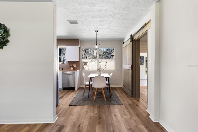 dining room featuring visible vents, a textured ceiling, light wood-style floors, and a barn door