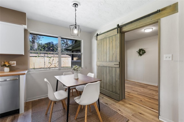 dining area with a barn door, baseboards, light wood-type flooring, and a textured ceiling