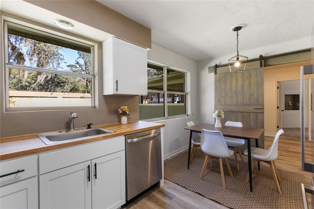 kitchen featuring dishwasher, a barn door, hanging light fixtures, white cabinetry, and a sink