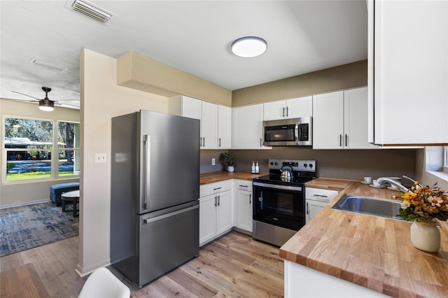 kitchen featuring visible vents, a sink, stainless steel appliances, butcher block countertops, and white cabinetry