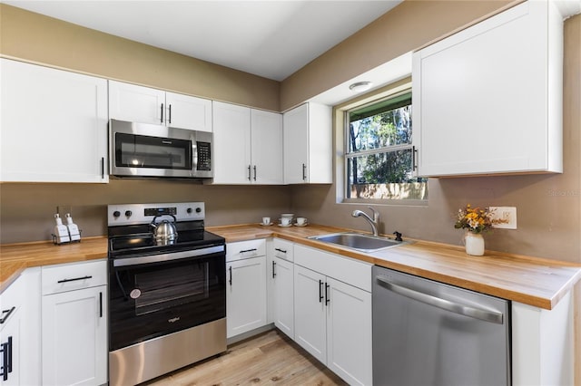 kitchen with a sink, white cabinets, butcher block countertops, and stainless steel appliances