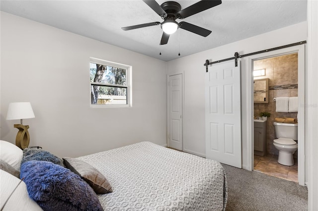 carpeted bedroom with ceiling fan, ensuite bath, and a barn door