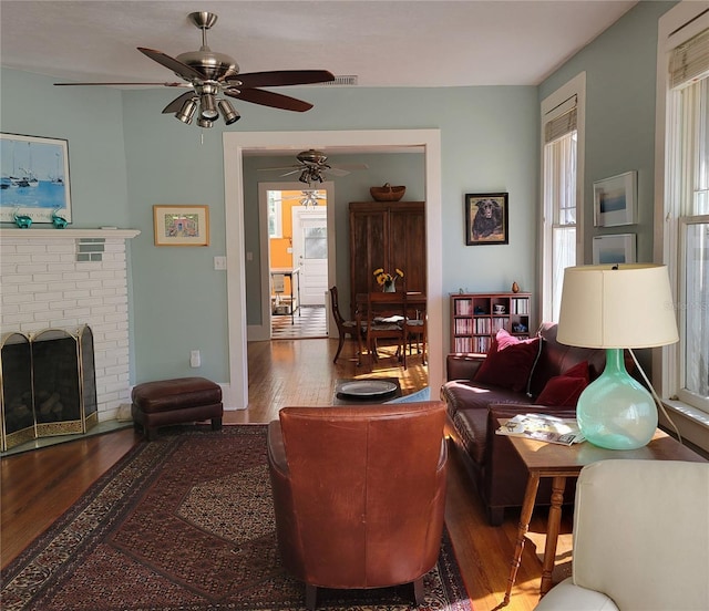 living area with a fireplace, wood finished floors, and a ceiling fan
