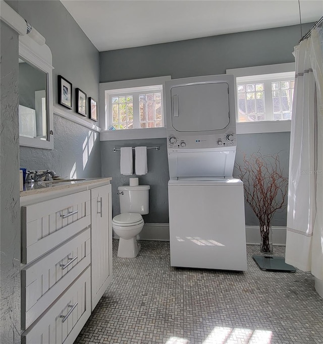 bathroom with toilet, vanity, baseboards, and stacked washing maching and dryer