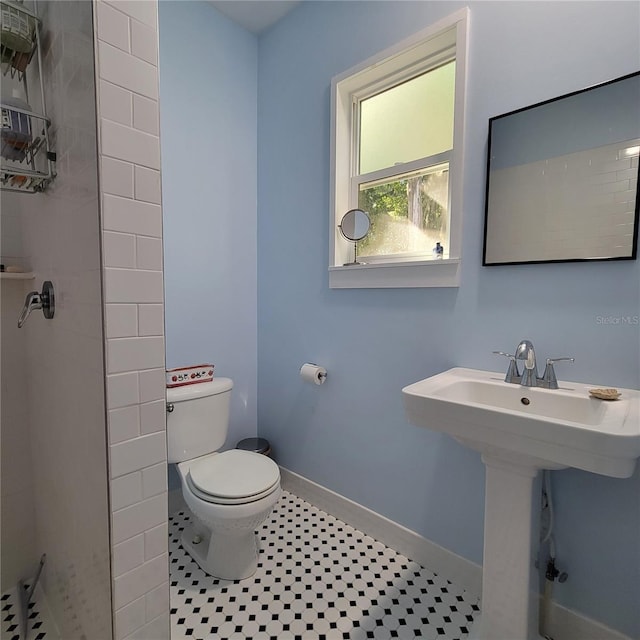 bathroom with tile patterned floors, a tile shower, toilet, a sink, and baseboards