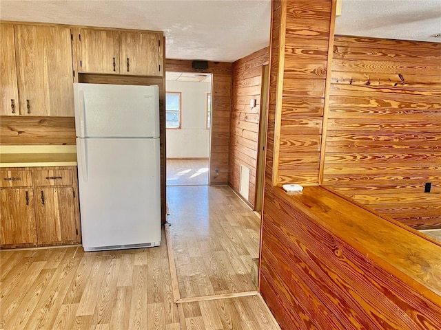 kitchen with light wood finished floors, wood walls, freestanding refrigerator, and a textured ceiling