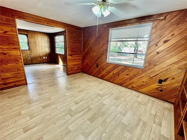 empty room featuring a ceiling fan, wood finished floors, and wood walls