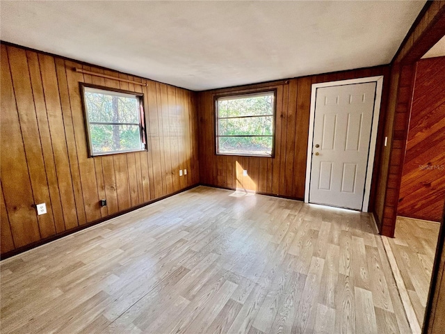 unfurnished room with wooden walls, light wood-style floors, and baseboards