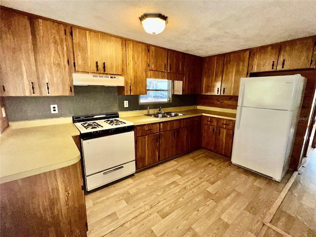 kitchen featuring under cabinet range hood, light countertops, light wood-style floors, brown cabinetry, and white appliances