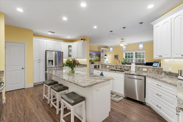 kitchen with a sink, a kitchen island, a peninsula, stainless steel appliances, and dark wood-style flooring