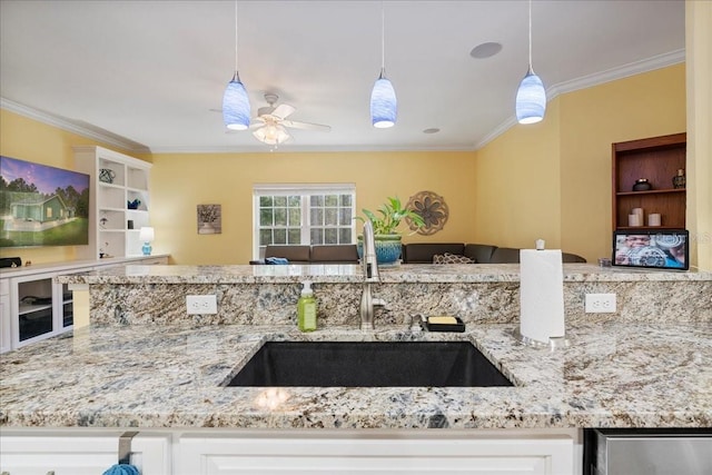 kitchen with a sink, light stone countertops, ornamental molding, and ceiling fan