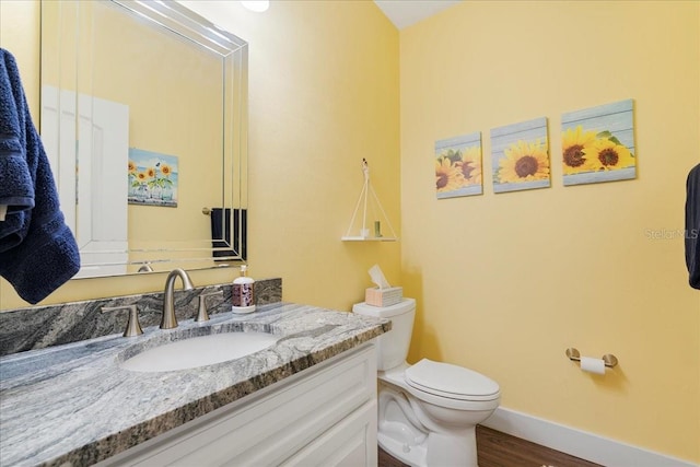 bathroom with baseboards, toilet, wood finished floors, and vanity