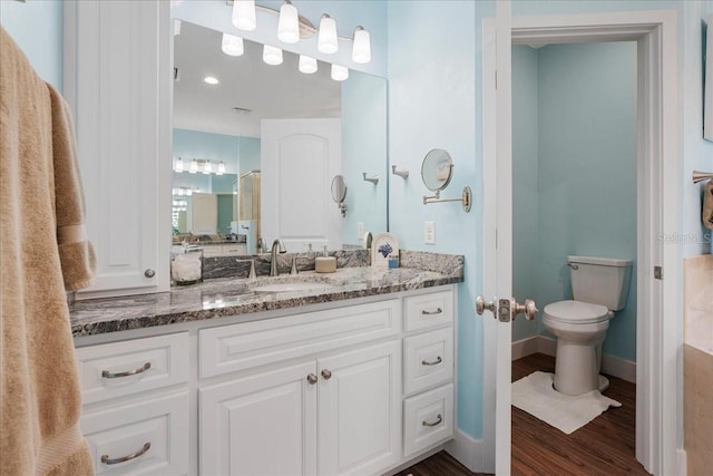 bathroom with baseboards, toilet, wood finished floors, a shower with shower door, and vanity