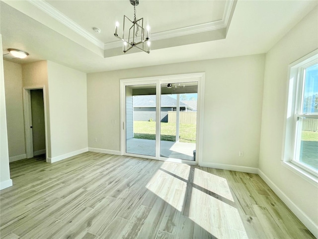 unfurnished room with a tray ceiling, plenty of natural light, an inviting chandelier, and light wood-style flooring