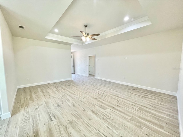 empty room featuring visible vents, a ceiling fan, baseboards, light wood-style floors, and a raised ceiling