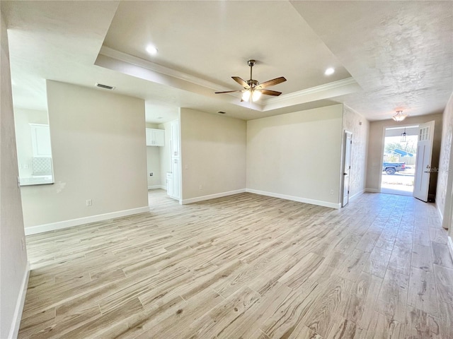 interior space with visible vents, baseboards, light wood-type flooring, a tray ceiling, and a ceiling fan