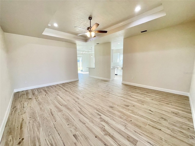 spare room with baseboards, ornamental molding, light wood-style flooring, a raised ceiling, and a ceiling fan