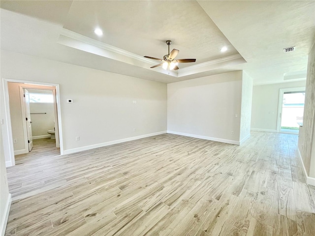 empty room with a tray ceiling, light wood-style floors, baseboards, and ornamental molding