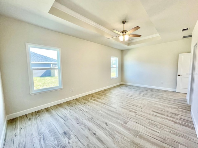 unfurnished room with visible vents, baseboards, light wood-type flooring, a tray ceiling, and a ceiling fan