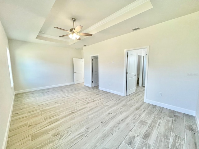 empty room with visible vents, light wood-style flooring, a tray ceiling, baseboards, and ceiling fan