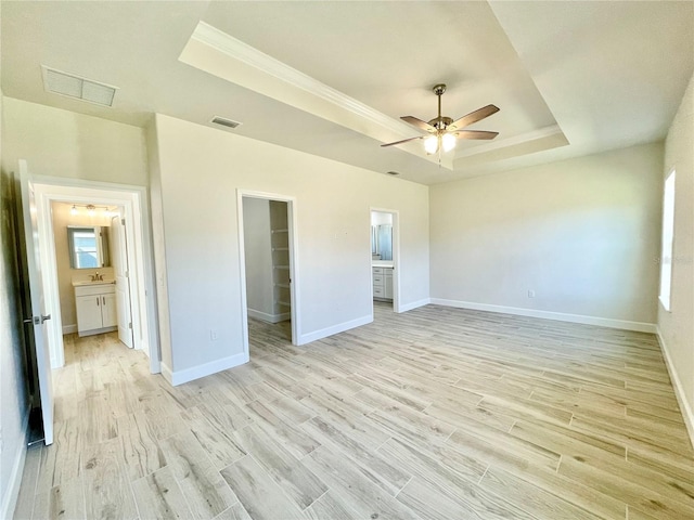 unfurnished bedroom featuring visible vents, a walk in closet, a raised ceiling, and light wood-style floors