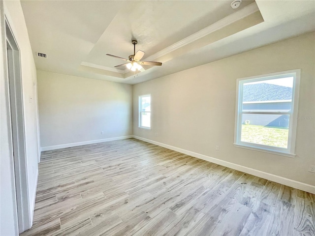 empty room featuring baseboards, a raised ceiling, light wood-style floors, and a ceiling fan