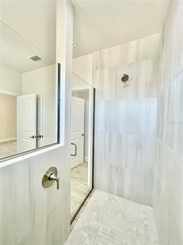 full bath featuring visible vents, tiled shower, and wood finished floors