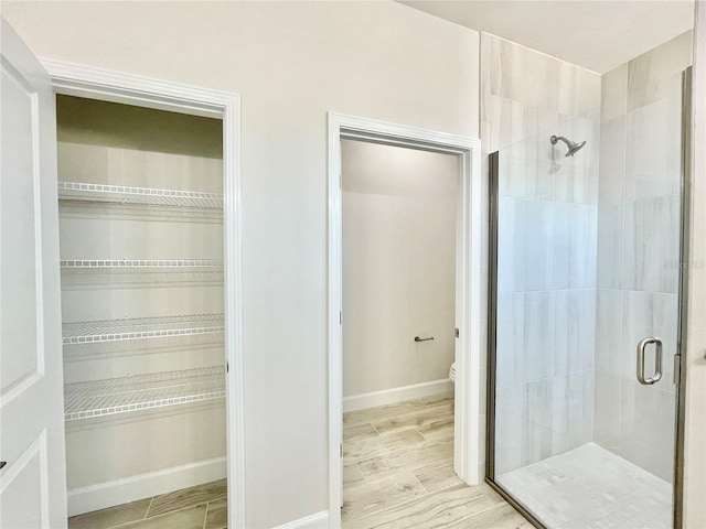 interior space with toilet, baseboards, a stall shower, and wood tiled floor