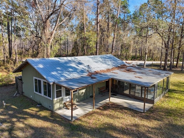 back of house featuring an attached carport, a forest view, metal roof, a yard, and a patio area