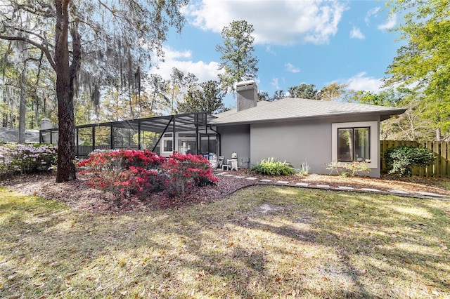 rear view of property featuring glass enclosure, fence, a yard, a chimney, and stucco siding