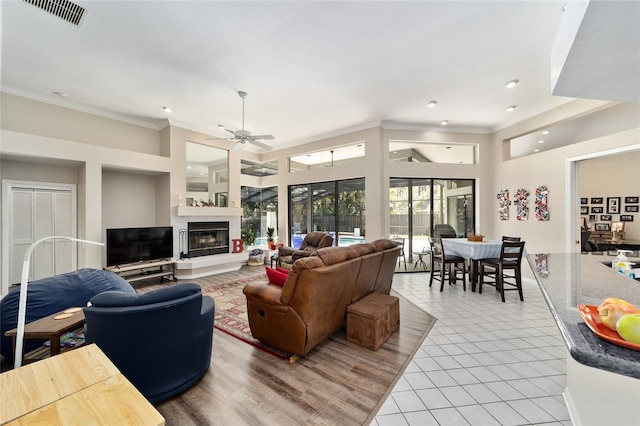 living area with visible vents, ornamental molding, a ceiling fan, a glass covered fireplace, and light tile patterned flooring