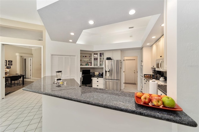 kitchen featuring white microwave, a peninsula, a tray ceiling, recessed lighting, and stainless steel fridge with ice dispenser