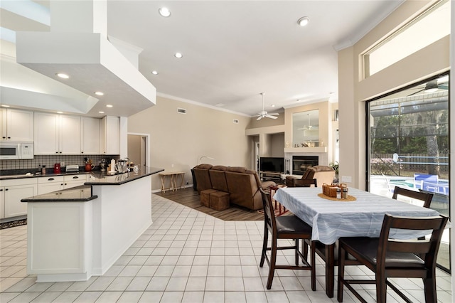 kitchen with ornamental molding, a ceiling fan, dark countertops, a glass covered fireplace, and white microwave