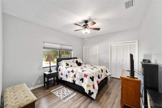 bedroom featuring visible vents, two closets, baseboards, and wood finished floors