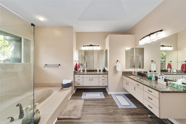 bathroom featuring a bath, a sink, two vanities, and wood finished floors