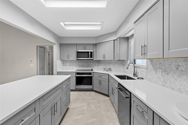 kitchen featuring gray cabinets, a sink, decorative backsplash, light countertops, and appliances with stainless steel finishes